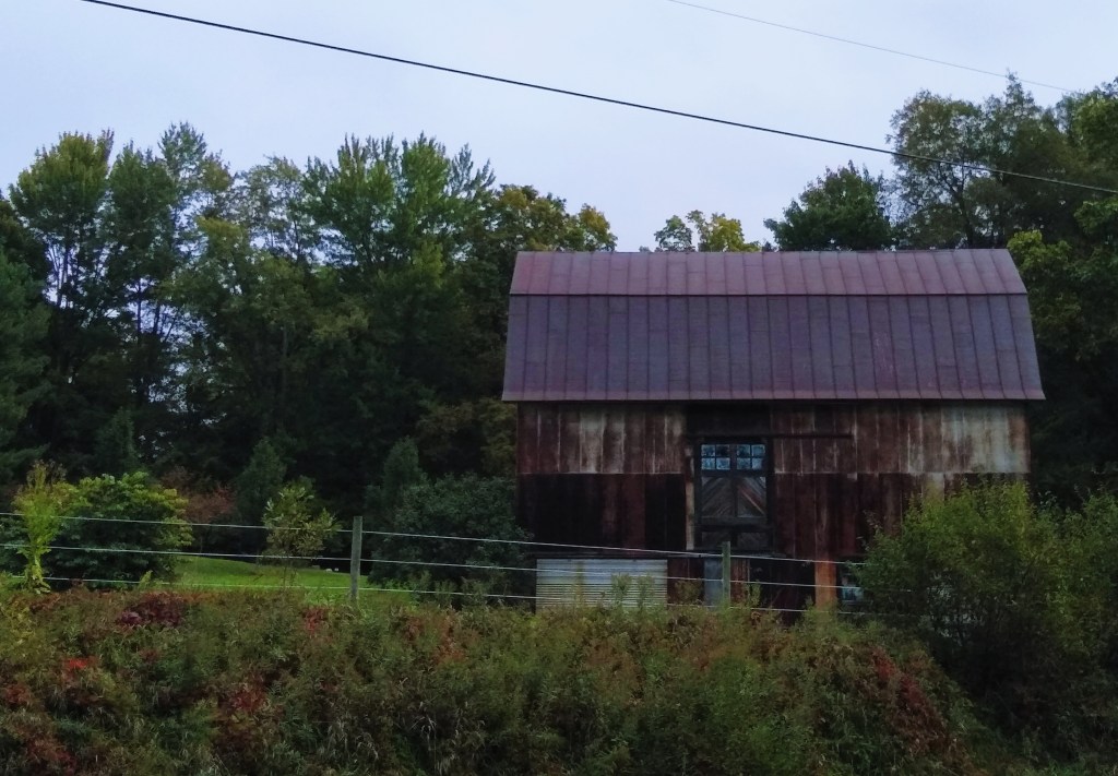 A rusted old metal sided barn at the side of the road.